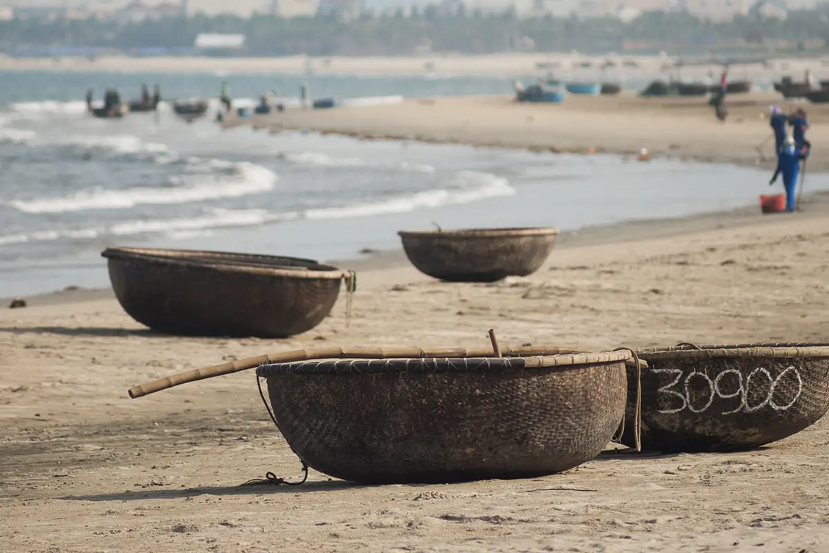 Round woven basket boats resting on a sandy beach, with surf and distant figures behind them