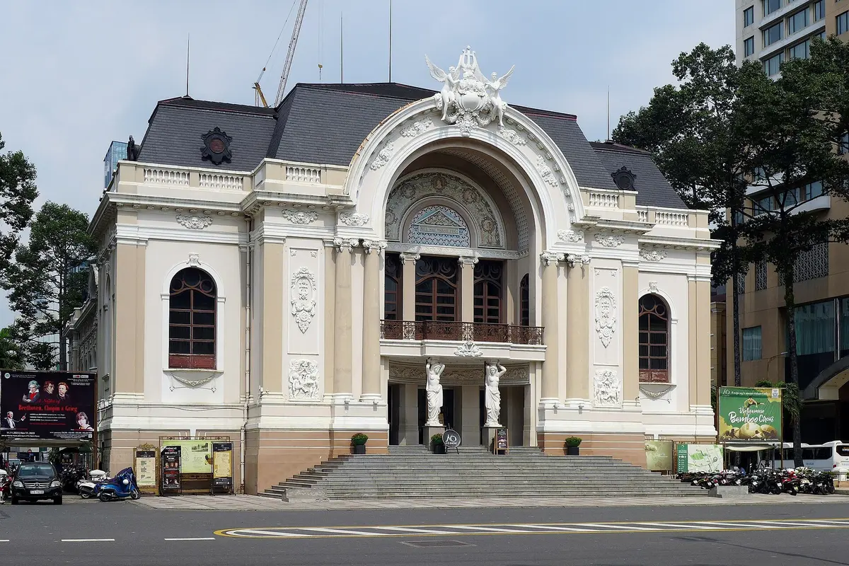 The cream-coloured Saigon Opera House seen from across the street, with its arched entrance, statues beside the doors and a grey roof